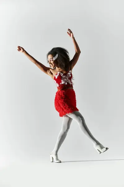 A young woman showcases her style in a bold red outfit, playfully posing against a soft grey backdrop. — Stock Photo