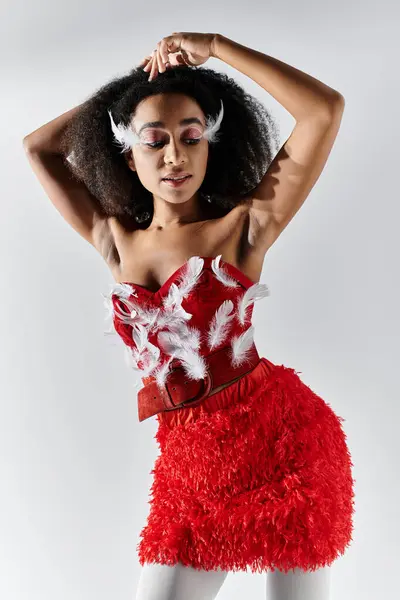 Une jeune femme élégante met en valeur sa tenue rouge unique, ornée de plumes, frappant une pose sur un fond gris. — Photo de stock