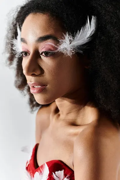 A stylish young woman showcases her unique red ensemble with feathers against a muted grey background. — Stock Photo