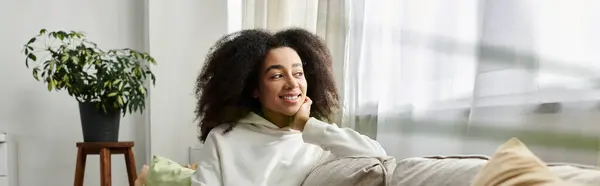 A joyful young woman relaxes at home, embracing the comfort of her cozy outfit in the living room. — Stock Photo