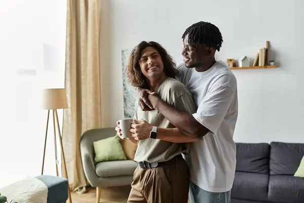 Two partners share a warm embrace while laughing, sipping coffee, and enjoying their home. — Stock Photo