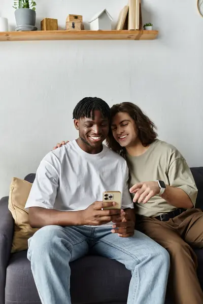 Two men embrace each other while smiling at their phone, enjoying a tender moment together. — Stock Photo