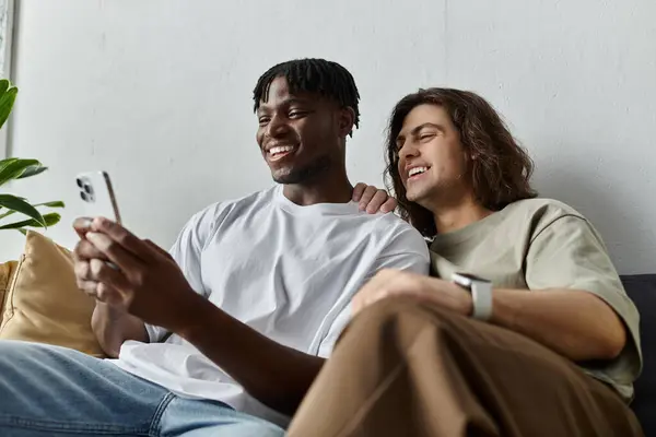 Two partners sit closely on a sofa, sharing a joyful moment as they look at a phone screen. — Stock Photo
