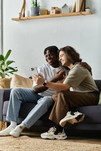 Two men embrace and laugh while looking at a phone on their cozy couch in a bright room. — Stock Photo