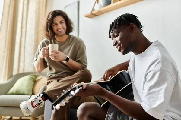 Two partners share a cozy moment, one strumming a guitar while the other relaxes with a drink. — Stock Photo