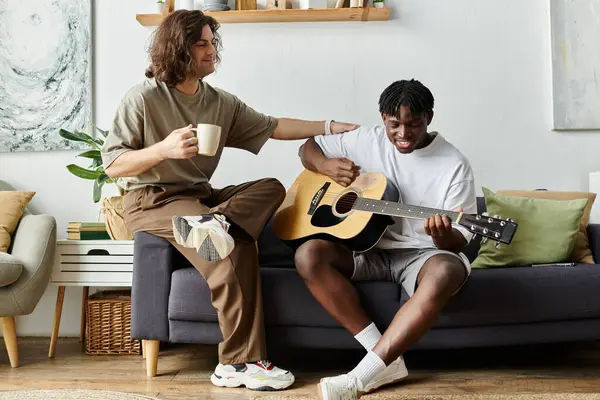 A happy couple share a tender moment while one strums a guitar and the other sips coffee. — Stock Photo