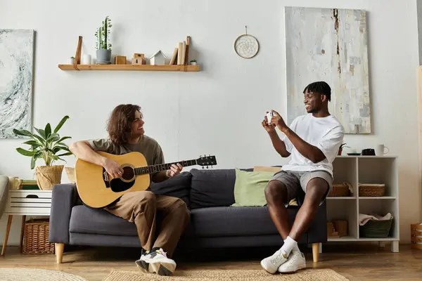 Two partners share a joyful moment as one plays guitar and the other captures the fun on camera. — Stock Photo