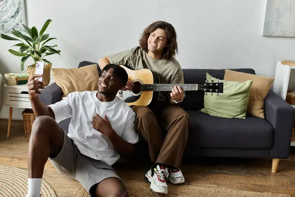 Due partner condividono un momento giocoso mentre uno suona la chitarra mentre l'altro cattura il divertimento su un telefono. — Stock Photo