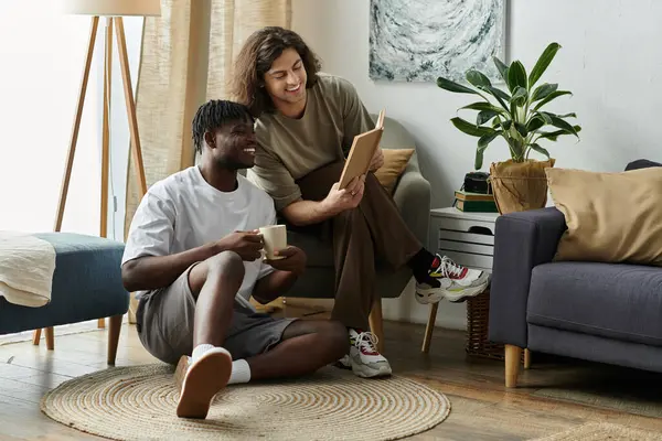 Dois parceiros compartilham um momento tranquilo em casa, sorrindo e lendo em seu espaço acolhedor juntos. — Stock Photo