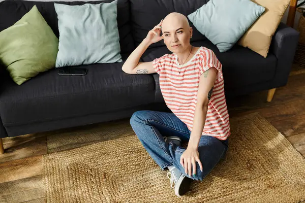 A young bald woman sits comfortably on the floor, reflecting in a warm, inviting space. — Stock Photo