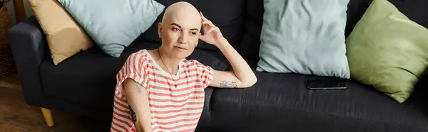 A young woman with alopecia sits on a sofa, thoughtfully gazing in her colorful space. — Stock Photo