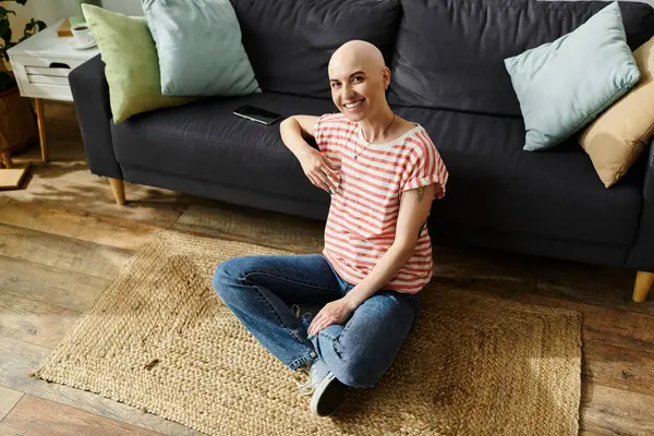 A young woman with a bald head smiles while seated comfortably on a woven rug. — Stock Photo