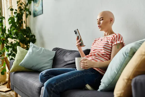 Una joven confiada con alopecia disfruta de un momento de relajación, sorbiendo té y desplazándose. — Stock Photo