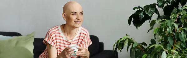 A bald woman relaxed on a couch, holding a cup while smiling at the greenery around her. — Stock Photo