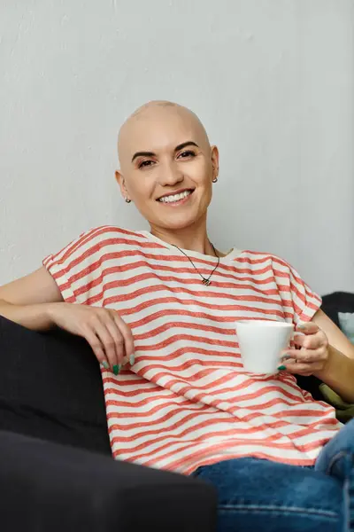 A joyful young woman with a shaved head smiles warmly while holding a cup of coffee. — Stock Photo