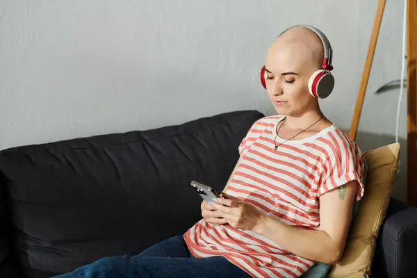 A young bald woman listens to music softly on headphones, lost in her thoughts on a sofa. — Stock Photo