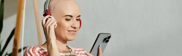 A young woman with alopecia smiles as she listens to music on her phone, enjoying her moment. — Stock Photo