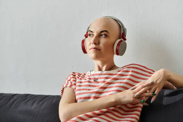 A young woman with alopecia listens to music, immersed in her thoughts, in a tranquil space. — Stock Photo