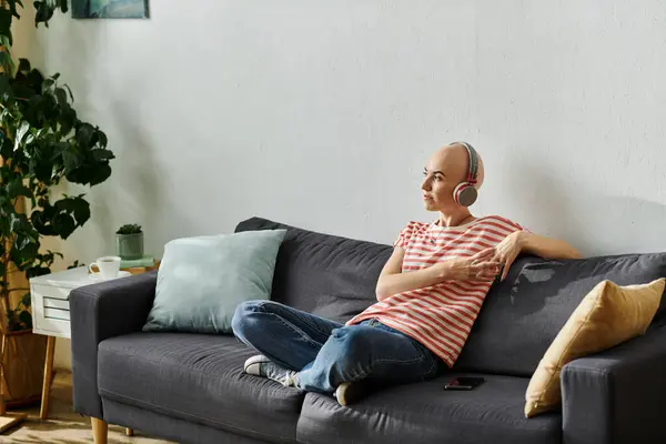 A bald woman with alopecia sits comfortably on a sofa, immersed in her music. — Stock Photo