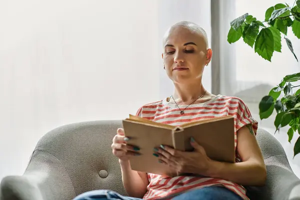 A young woman with alopecia reads intently while relaxing in a sunlit room. — Stock Photo