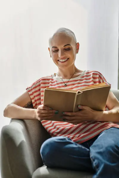 A bald woman enjoys a book on a cozy couch, smiling as sunlight warms her serene space. — Stock Photo