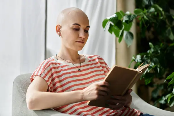Молодая женщина с алопецией мирно читает книгу в удобном кресле посреди зелени. — стоковое фото