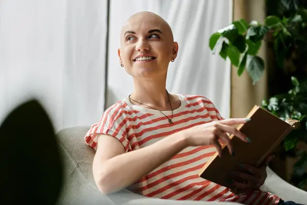 A joyful bald woman relaxes on a couch, immersed in a book and appreciating her surroundings. — Stock Photo