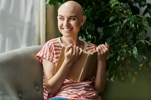 Una joven y hermosa mujer calva sonríe brillantemente mientras escribe en su diario, rodeada de vegetación. - foto de stock