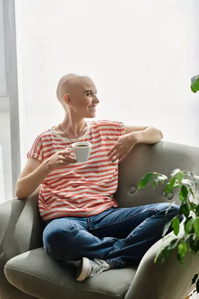 A young bald woman sits calmly on a couch, savoring tea and sunshine in her cozy space. — Stock Photo