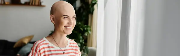 A young woman with a bald head radiates positivity while standing by the window. — Stock Photo