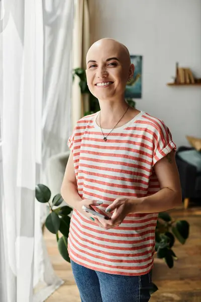 A warm and inviting moment as a bald woman holds her phone, exuding positive energy indoors. — Stock Photo