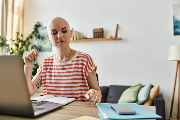 A bald woman thoughtfully marks notes in her journal while seated at a wooden desk. — Stock Photo