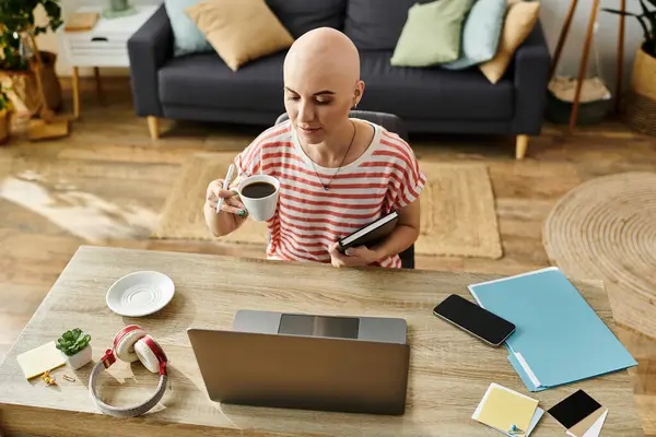 A beautiful young woman with alopecia sips coffee while reviewing notes at her desk. — Stock Photo