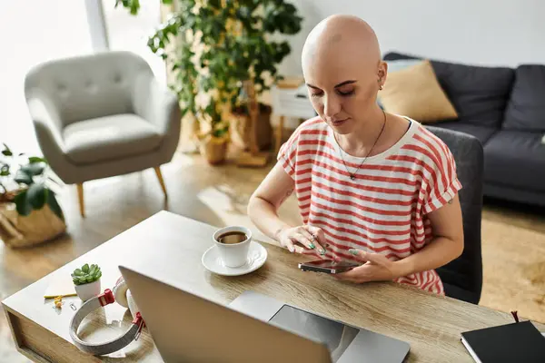 A beautiful bald woman sits at a cozy table, focused on her smartphone with coffee nearby. — Stock Photo
