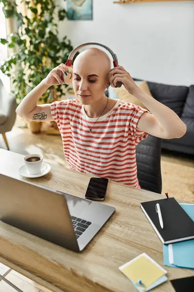 Una bella donna calva si siede comodamente, si concentra sul suo lavoro, indossa cuffie e sorseggia caffè. — Foto stock