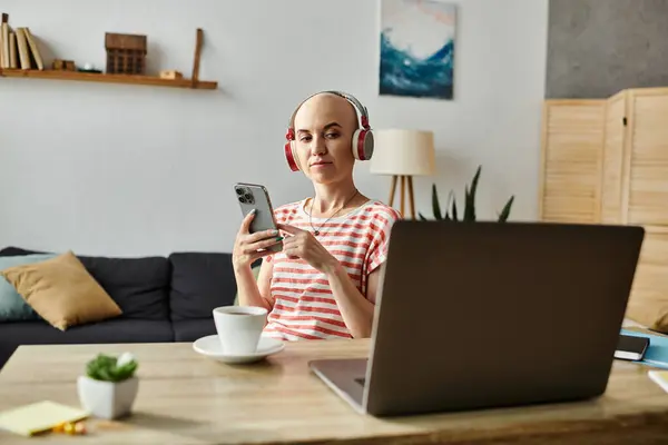 Una giovane donna con l'alopecia si rilassa con il caffè e il suo telefono, godendo la musica. — Foto stock