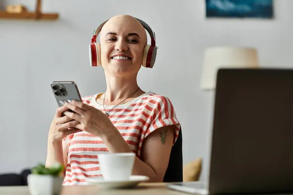 A young bald woman smiles while listening to music on her headphones, holding her smartphone. — Stock Photo
