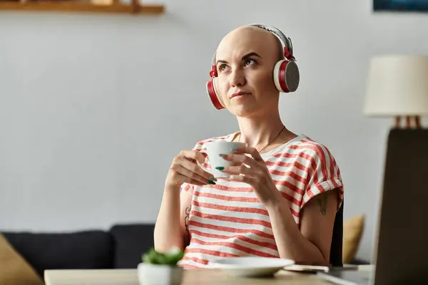 A young, bald woman relaxes with a warm drink, lost in thought while listening to music. — Stock Photo