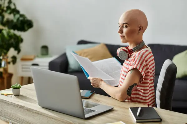 Une jeune femme chauve atteinte d'alopécie est engagée dans la lecture de matériel assis à son bureau. — Photo de stock