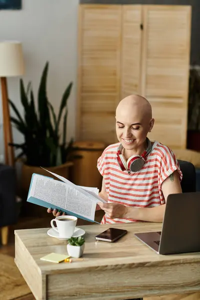A bald woman sits at a desk, smiling as she reads a book and enjoys her coffee in a bright space. — Stock Photo