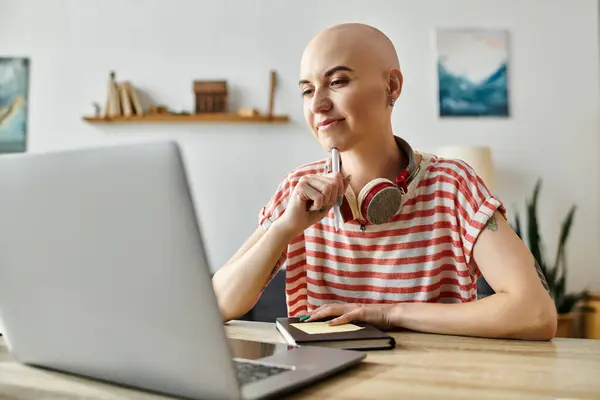A beautiful bald woman with alopecia thoughtfully works on her laptop while surrounded by books. — Stock Photo