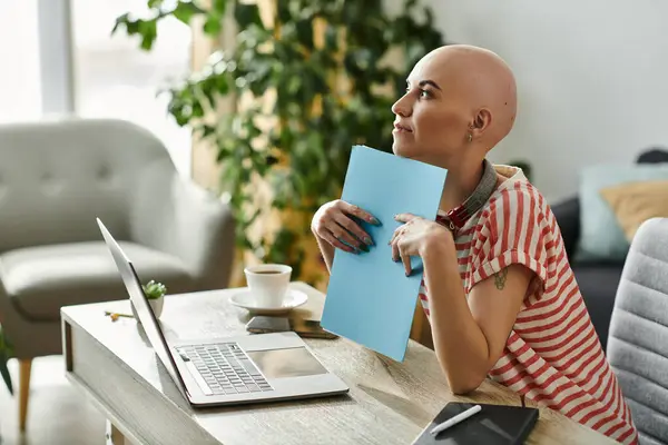 Una joven calva se sienta en su escritorio, sosteniendo una carpeta azul y mirando pensativamente hacia adelante. — Stock Photo