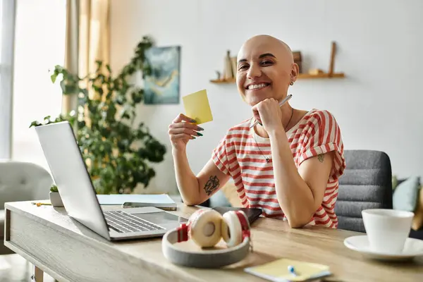 Eine fröhliche Frau mit Glatze beschäftigt sich mit ihrem Arbeitsplatz, umgeben von Pflanzen und einem Laptop. — Stockfoto