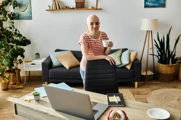 A young bald woman savors a warm drink while standing in her stylish workspace. — Stock Photo