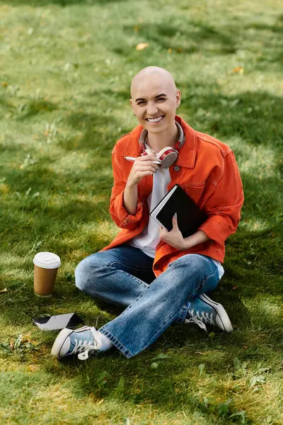 A joyous young bald woman enjoys a sunny afternoon, sipping coffee and writing. — Stock Photo