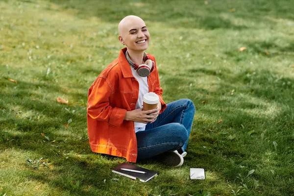 A vibrant young woman with alopecia sits on the grass, smiling and enjoying her coffee. — Stock Photo