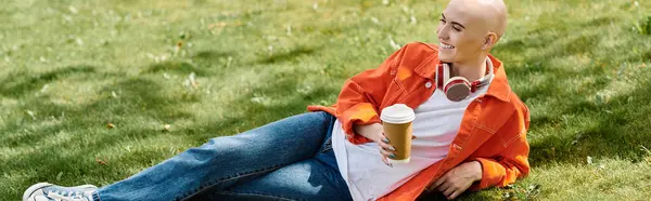 A young bald woman lounges on the grass, sipping coffee and soaking up the sun. — Stock Photo