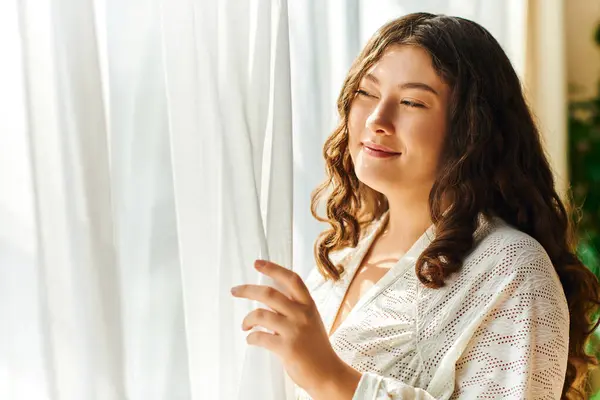 The radiant woman savors the sunlight streaming through the curtains, enjoying a peaceful moment. — Stock Photo