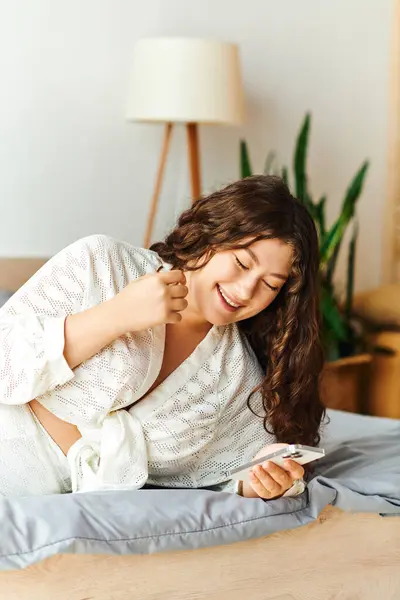 A young beautiful plus size woman laughs while lounging at home, engaging with her smartphone. — Stock Photo