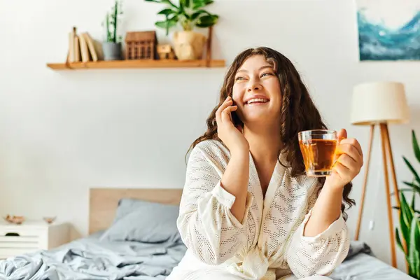 A young woman relaxes at home, sipping tea and chatting happily, wrapped in comfort. — Stock Photo